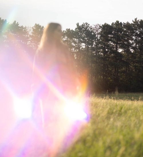Frau steht auf Wiese, wird von einer bunten lichtspiegelung verdeckt